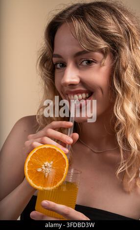 Junge Frau genießt ein Glas frischen Orangensaft mit einer Orangenscheibe, fühlt sich gesund und erfrischt Stockfoto