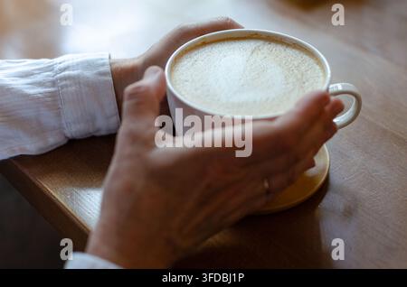 Nahaufnahme von Händen, die eine weiße Tasse Cappuccino halten Stockfoto