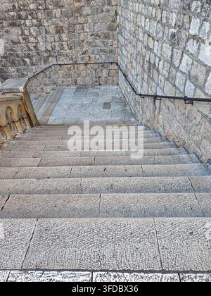 Blick hinunter eine Reihe verwitterter Steinstufen, die von alten Festungsmauern und Metallgeländern in den Stadtmauern von Dubrovnik umgeben sind. Stockfoto