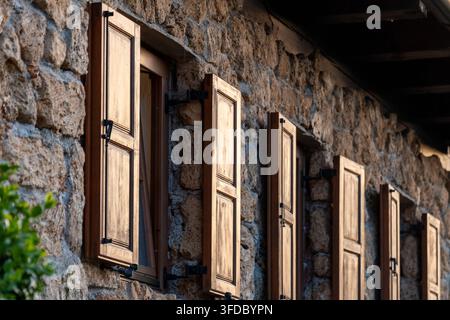 Sonnenbeschienene Holzläden säumen eine rustikale Steinmauer an einem alten Haus. Stockfoto