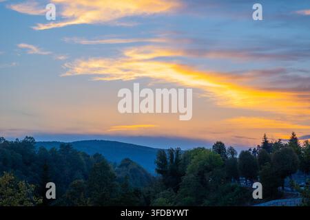 Dramatischer Sonnenuntergangshimmel, der über bewaldeten Hügeln und einem Tal leuchtet Stockfoto