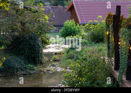 Friedlicher Gartenbach windet sich neben rustikalen Häusern im sanften Abendlicht Stockfoto