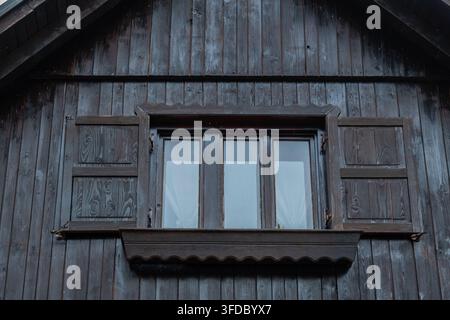 Rustikale dunkle Holzfassade mit verschlossenem Fenster und dekorativer Blumenkiste Stockfoto