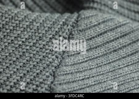 Grauer gestrickter Wollstoff, der eine strukturierte Oberfläche mit verschiedenen Stichmustern zeigt Stockfoto