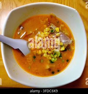 Leckere japanische Miso-Ramen-Nudeln serviert in einer weißen Schüssel, belegt mit süßer Maiskolben, geschnittenem Chashu-Schinken, grüner Zwiebel und roten Chilifäden in Stockfoto