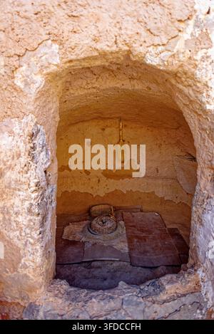 Eine Innenansicht, die durch eine gewölbte Lehmziegelöffnung in eine spezielle Schleifnische mit einer antiken Handsteinmühle in Dar Taoufik blickt Stockfoto