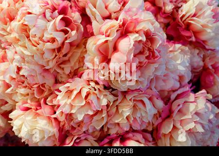 Nahaufnahme von geschichteten rosa und cremefarbenen künstlichen Blütenblättern, die eine weiche, gerüschte Florale Textur in warmem natürlichem Licht bilden. Stockfoto