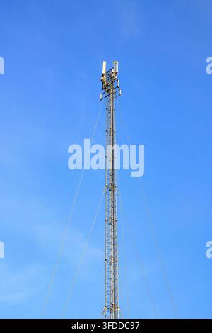 Hoher Metallgitter-Funkmast mit Panelantennen, die von Spannseilen gehalten werden, unter einem strahlend blauen Himmel. Konzept von drahtlosen Netzen, Zelle Stockfoto