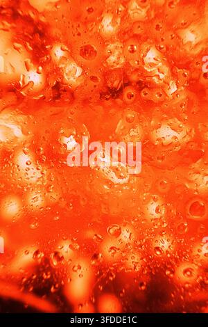 kühle Kondensation auf einer Glasoberfläche mit Wassertropfen in einer rot-orangen Umgebung, Nahaufnahme von oben, kommerzielles natürliches Licht, sauberer Hintergrund Stockfoto