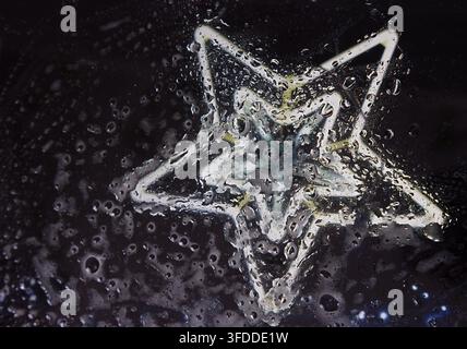 Regentropfen auf dem Glas vor einem dunklen Hintergrund, mit einem leuchtenden Stern, mit schwarzen, weißen Akzenten und stimmungsvoller reflektierender Stimmung, nahegelegene Objekte, umgeben Stockfoto