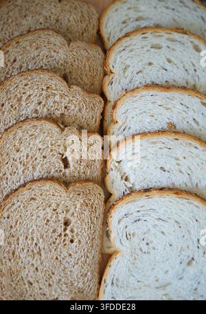 Geschnittenes dunkles und helles Brot gestapelt und angeordnet, in einem Innenraum, wahrscheinlich in einer Küche oder Bäckerei, mit Scheiben von Weißbrot, Scheiben von Vollkornbrot, von oben Stockfoto