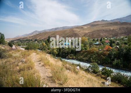 Ein gewundener Fluss fließt durch ein Tal, in dem sich eine Ansammlung von Häusern mit bunten Dächern zwischen grünen und gelben Bäumen schmiegt. Trocken, braun-grüne Hügel Stockfoto