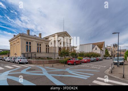 Breitwinkelansicht des neoklassizistischen Gerichtsgebäudes Palais de Justice in Louviers, Frankreich, mit seinem säulengeschmückten Portikus, geparkten Autos und der gotischen Kollegiatkirche Stockfoto