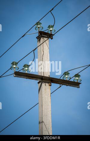 Ein Beton-Mast steht vertikal mit vier sichtbaren grünen Glasisolatoren, zwei oben und zwei auf einem Metallquerspann, die eine Leitung tragen Stockfoto