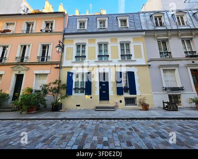Farbenfrohe historische Wohnhäuser mit blauen Fensterläden und eine Kopfsteinpflasterstraße entlang der Rue Crémieux in Paris, Frankreich. Stockfoto