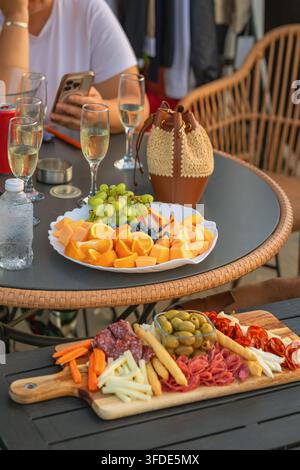 Schinkenteller und frisches Obst bei einer Versammlung im Freien. Schinkenteller mit gepökeltem Fleisch, Käse, Oliven, Brotscheiben, serviert mit frischem Obst Stockfoto