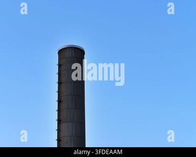 Detaillierte Aufnahme eines hohen zylindrischen industriellen Metallschornsteins mit angebrachter Wartungsladder. Die Struktur steht vertikal vor einem Vi Stockfoto