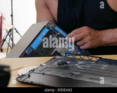 Detaillierte Nahaufnahme der Hände einer Person, die ein schwarzes Tanktop trägt und sorgfältig interne Komponenten wie den Kühlventilator und die blauen Lamellen des entfernt Stockfoto