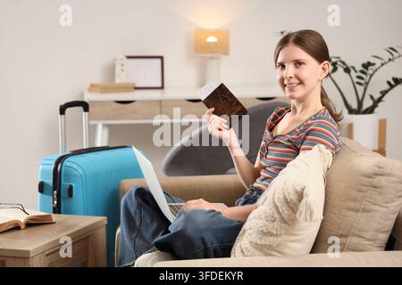 Digital-Nomad-Lebensstil und Reiseplanung, junge Frau mit Laptop und Reisepass bereitet sich in einem Homeoffice auf den Urlaub vor, mit gepacktem Gepäck bereit zum Aufbruch Stockfoto