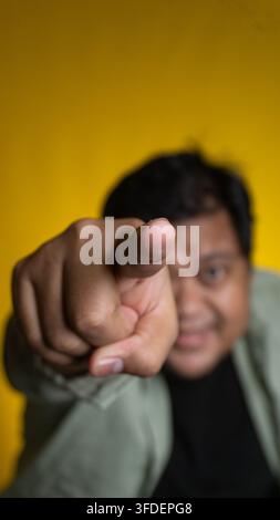 Eine extreme Nahaufnahme hebt einen einzelnen Finger hervor, der gerade nach vorne zeigt, während das stark unscharfe Gesicht eines jungen asiatischen Mannes im Hintergrund sanft lächelt Stockfoto