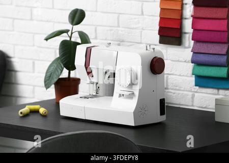 Nähmaschine mit Garnspulen und Pflanze auf dem Schneider Tisch im Atelier, Nahaufnahme Stockfoto