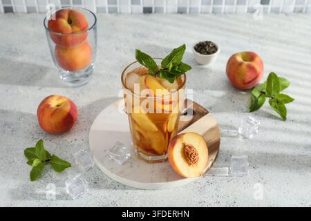 Glas leckerer Pfirsicheistee auf grauem Grunge-Hintergrund, Nahaufnahme Stockfoto