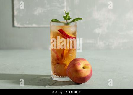 Glas leckerer Pfirsicheistee auf grünem Grunge-Hintergrund, Nahaufnahme Stockfoto