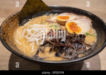 Nahaufnahme einer japanischen Ramenschüssel mit cremiger Tonkatsu-Brühe, Nudeln, geschnittenem Schweinefleisch Chashu, weich gekochten Eiern, Waldohrenpilzen, grünen Zwiebeln, einem Stockfoto