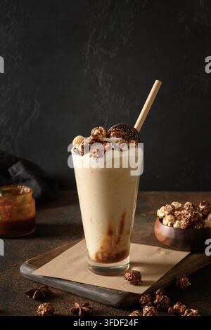 Leckerer Bananenmilchshake garniert mit Karamell, Schlagsahne, Popcorn auf dunklem Hintergrund. Vertikales Format Stockfoto