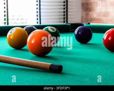 Nahaufnahme von Billardkugeln und Queue auf grüner Filzplatte. Ein selektiver Fokus auf farbenfrohe nummerierte Kugeln, die auf einem grünen Snookertisch verstreut liegen Stockfoto