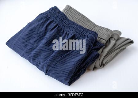 Gestapelte blaue und olivgraue Herren-Joggertrousers auf sauberem Hintergrund. Atmungsaktive Freizeit-Activewear, geeignet für Fitnessstudio-Workout, Laufen und Lounge Stockfoto