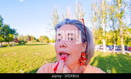 Reife Frau trägt im Park draußen Lippenstift auf Stockfoto