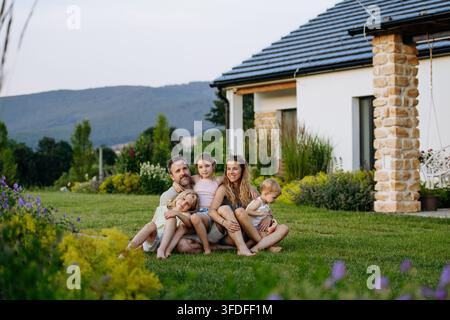 Familie genießt den Spätsommerabend zusammen in ihrem neuen Haus, sitzt auf dem Rasen. Stockfoto