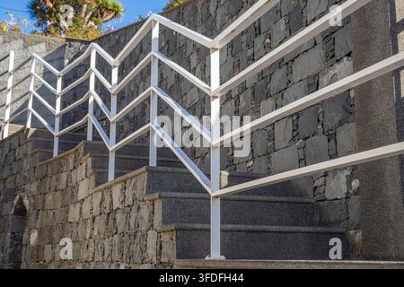 Steinerne Außentreppe mit weißen Metallgeländern neben einer strukturierten Mauer Stockfoto
