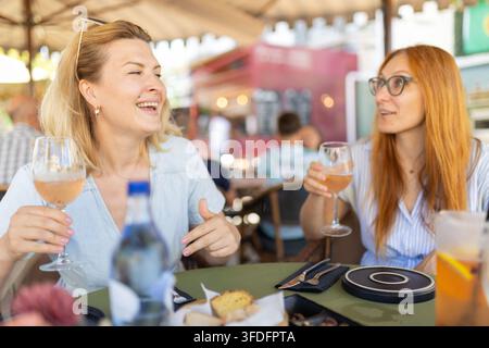 Zwei Freunde genießen Getränke und Essen in einem Straßencafé in einer geschäftigen städtischen Umgebung an einem sonnigen Tag Stockfoto