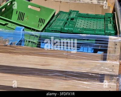 Hohe Blickwinkel-Aufnahme von grünen und blauen Plastikobstkisten, die in einer großen Holzpalettenbox gestapelt sind. Der gesamte Holzkontainer ist fest eingewickelt Stockfoto