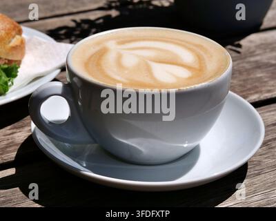 Nahaufnahme einer Tasse mit heißem Cappuccino, die schöne Herz- und Blatt-Latte-Art auf cremigem Milchschaum zeigt. Serviert in einer weißen Porzellantasse mit Untertasse Stockfoto