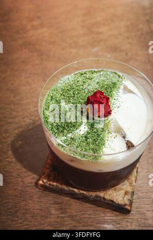 Eine Aufsichtaufnahme von dunklem Kaffee und weißem Milchschaum in einem durchsichtigen Glas. Die Oberfläche des Milchschaums ist mit smaragdgrünem Matcha-Pulver bestreut Stockfoto