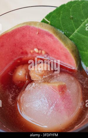 Das Glas enthält dunklen Eiskaffee und gewürfelten Eis. Eine halbmondförmige Wassermelone liegt am Rand des Glases, und ein großes grünes Perilla-Blatt ist Stockfoto
