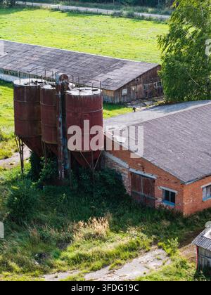 Luftaufnahme eines verlassenen landwirtschaftlichen Komplexes aus der Sowjetzeit mit verrosteten Silos und verfallenen Backsteingebäuden, umgeben von überwucherten Feldern in Kulcie Stockfoto