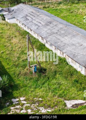 Luftaufnahme eines verlassenen landwirtschaftlichen Komplexes aus der Sowjetzeit mit einem verwitterten Dach und überwuchertem Gras in Kulciems, Gemeinde Talsi, Lettland. Stockfoto