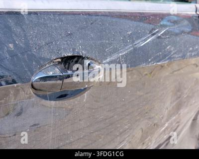 Detaillierte Aufnahme, die sich auf einen schwarzen Autotürgriff konzentriert, der mit Staub und Straßenschmutz bedeckt ist, umgeben von auffälligen Farbkratzern und Schrammen. Das Bild illus Stockfoto