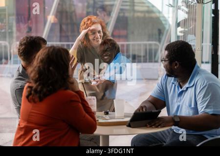 Lächelnde rothaarige Frau begrüßt Freunde in einem Café Stockfoto