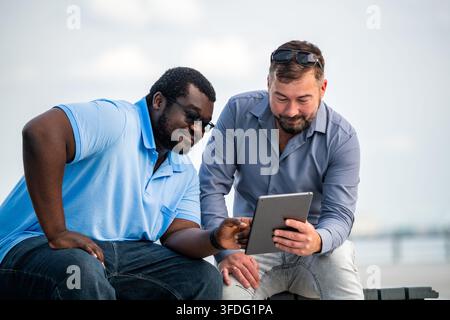 Zwei verschiedene männliche Freunde, die im Freien ein digitales Tablet verwenden Stockfoto