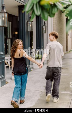 Junges Paar hält sich an den Händen, während es auf dem Gehweg spaziert Stockfoto