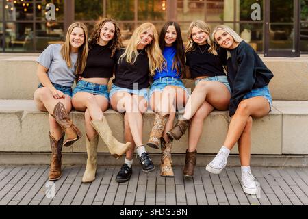 Glückliche junge Freunde in Cowboystiefeln sitzen zusammen Stockfoto