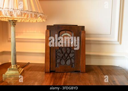 Ein vintage Holzradio steht auf einem Holztisch neben einer verzierten Lampe mit einem Fransenschirm. Die Bibliothek - Trent Park House - London Stockfoto