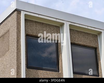 Nahaufnahme einer architektonischen Ansicht, die grobe freiliegende Betonplatten und dunkel gerahmte quadratische Fenster einer Retro-Vintage-Eckgebäude zeigt. Repr Stockfoto