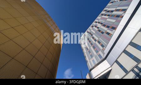 Eine eindrucksvolle Niedrigwinkel-Architekturansicht zeigt den Kontrast zwischen dem markanten goldverkleideten Turm und der gemusterten Glasfassade der Queen E Stockfoto
