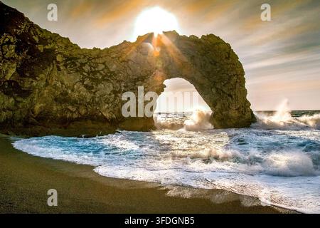 Sonnenuntergang über Durdle Door Dorset UK, während stürmische Meereswellen durch den Kalksteinbogen krachen Stockfoto